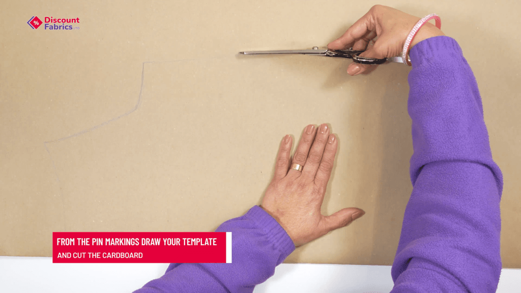 A person wearing a purple sleeve uses scissors to cut a design into brown cardboard. Their left hand holds the cardboard steady. There's a red text box that reads,