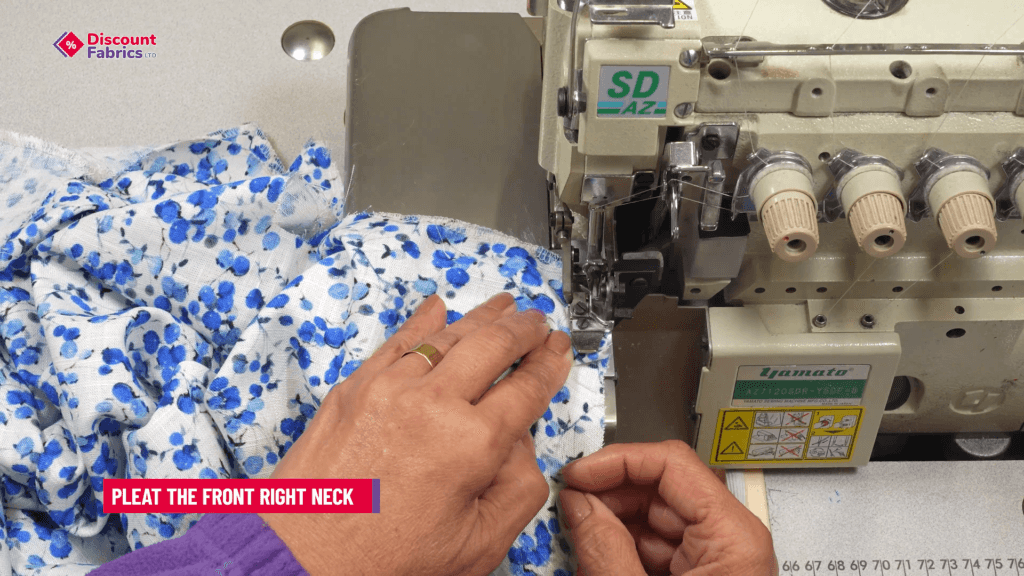 A person sewing a piece of white and blue floral fabric on an industrial sewing machine. A sign above reads
